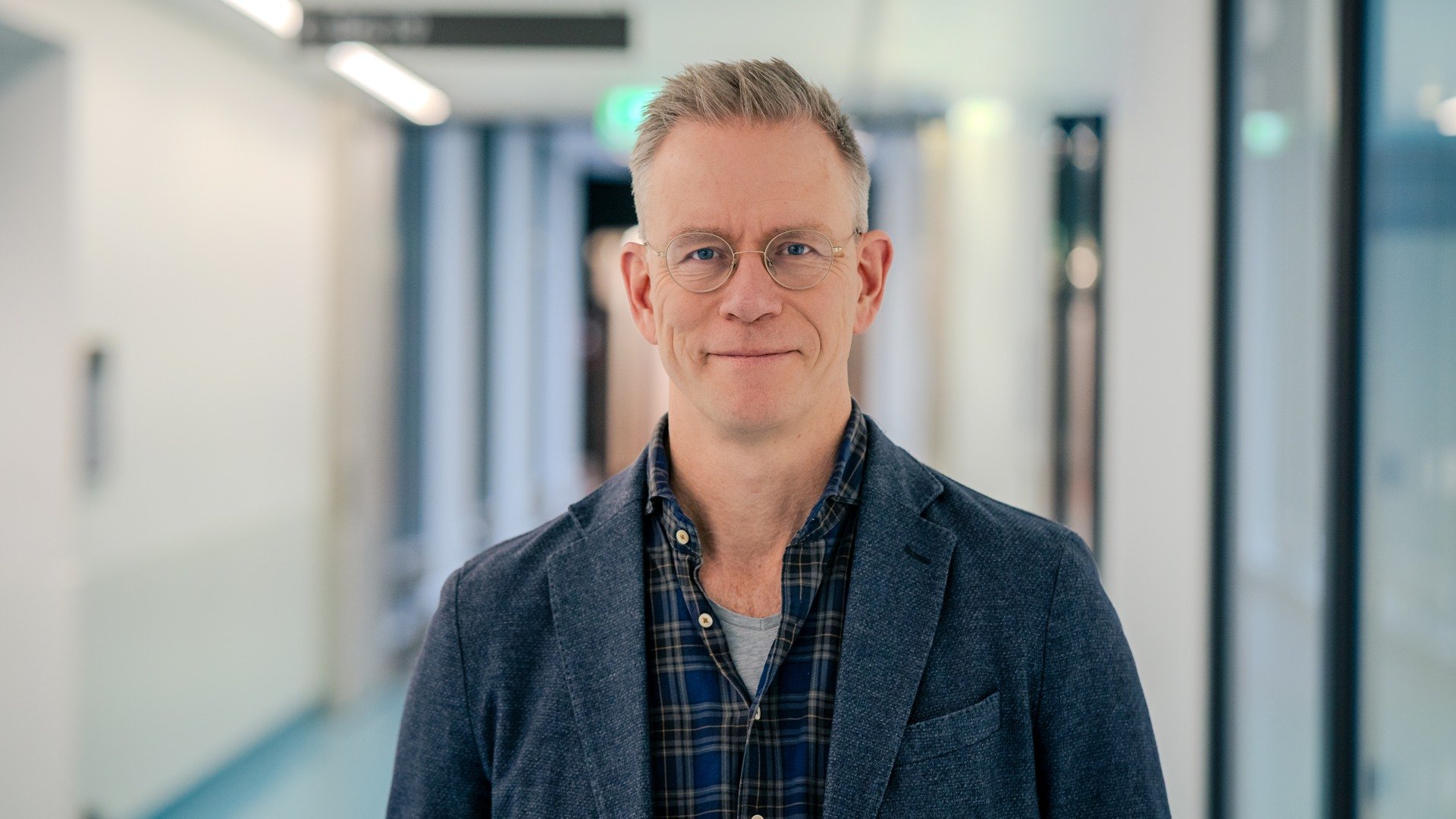 A man with glasses standing in a hallway.