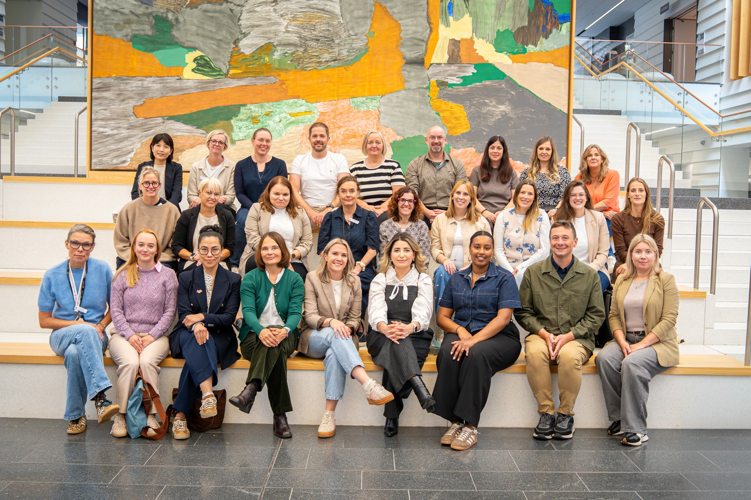 A group of people sitting and standing in front of a painting.