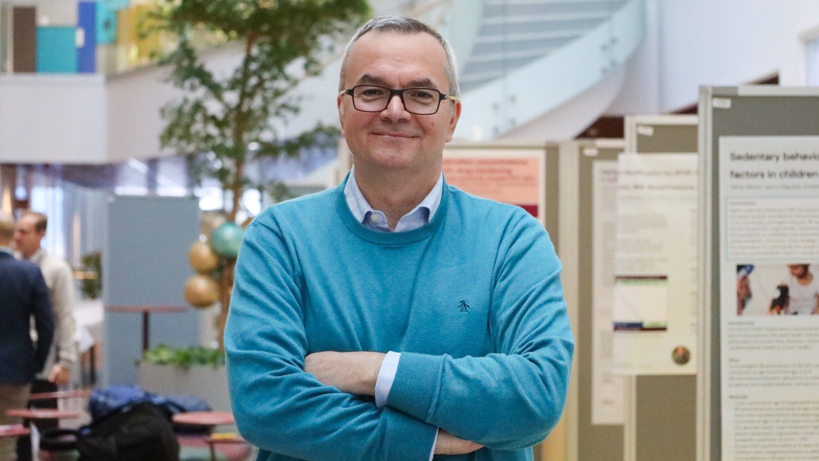A man in a blue sweater standing in front of a poster.