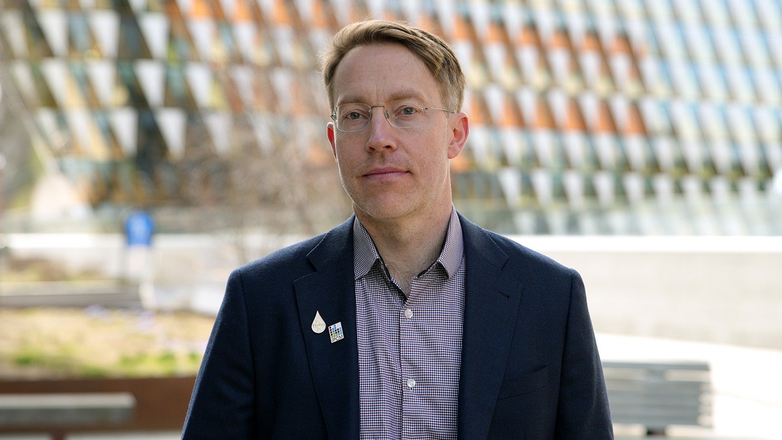 A man in a suit and glasses standing in front of a building.