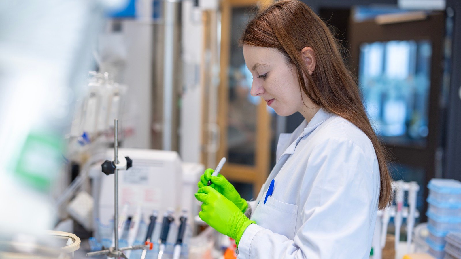 A woman in a lab coat and green gloves.