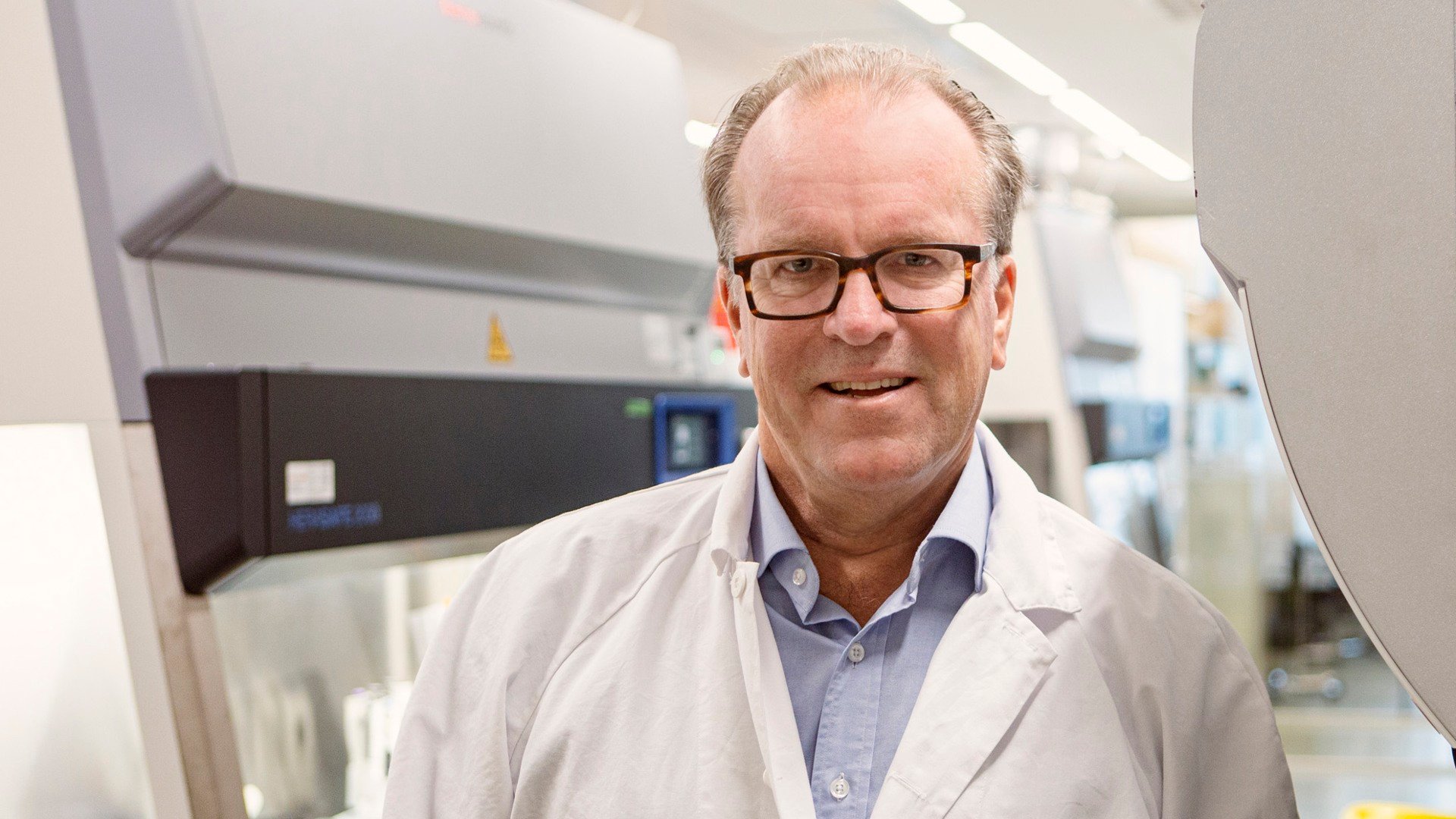 A man in a lab coat standing in front of a machine.