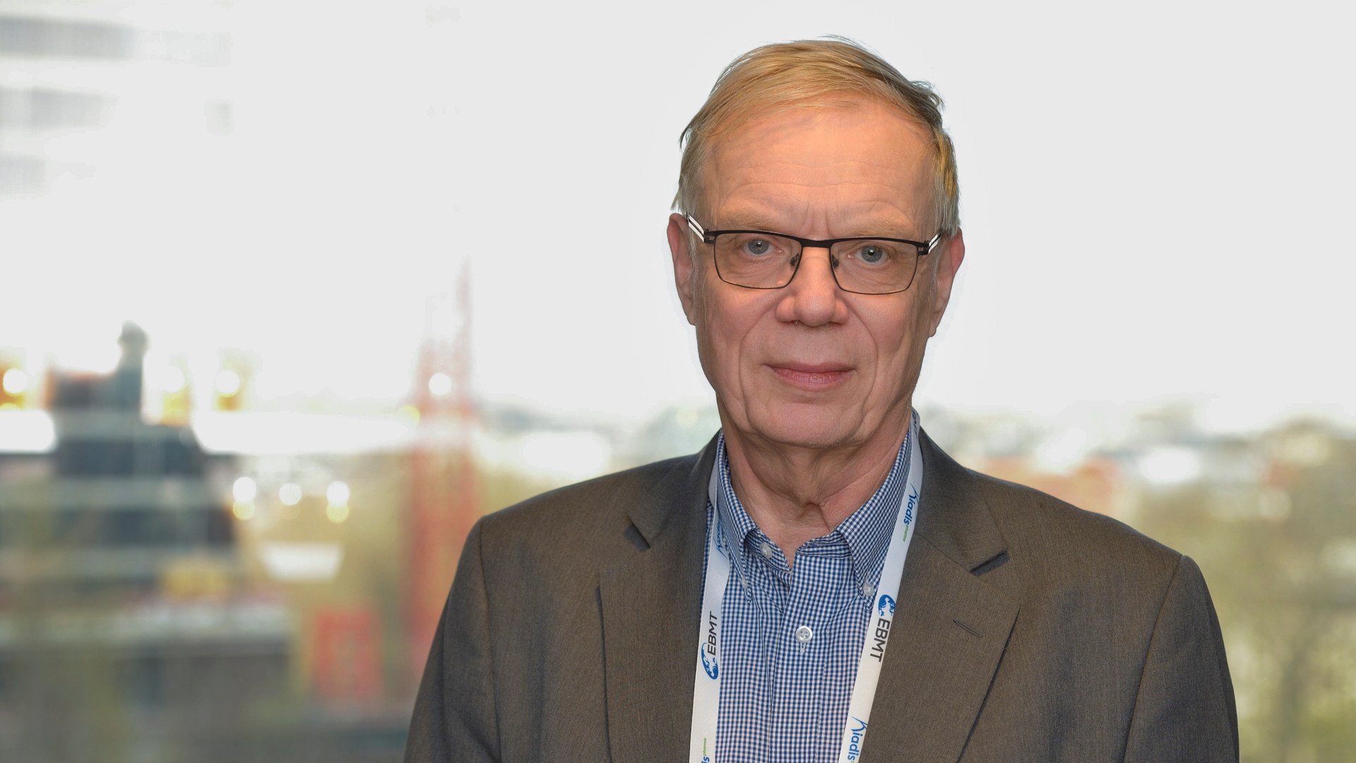 A man in a suit and glasses standing in front of a window.