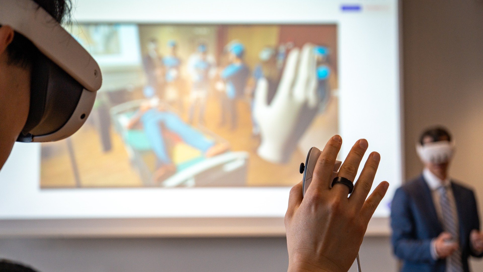 A person wearing a virtual headset in front of a projector screen.
